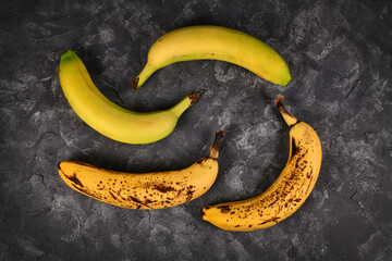 Comparison of ripe bananas with black patches and slightly green bananas on black background