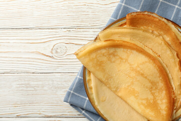 Kitchen towel with plate of thin pancakes on wooden background
