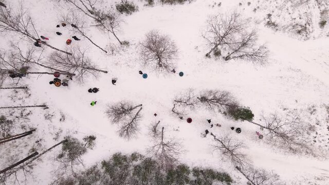 Adults and children move between trees with inflatable sleds. People ride tubing, cheesecakes from a snowy slope at a ski resort. Family vacation in the New Year's holidays in nature.