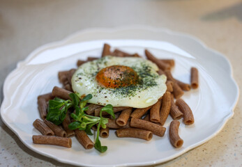 Fried egg with buckwheat noodles  and arugula on white plate