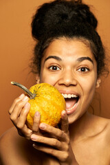 Fresh squash. Portrait of excited young mixed race female model looking at camera, holding little pumpkin, posing isolated over orange background. Healthy eating, skincare concept
