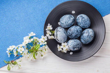 Easter blue marble eggs in a black plate with cherry flower on the white wooden table