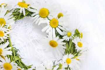 Obraz premium Wreath of chamomile flowers on white crochet napkin and white background, handmade vintage wreath of wild meadow flowers 