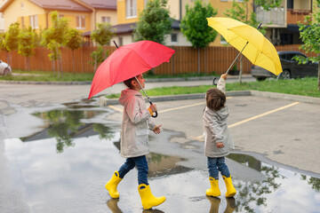 Children play with umbrellas after the rain in the street, run through puddles, have fun and play