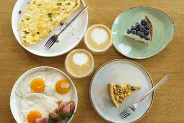 Bright breakfast on brown wooden background, top view. Tasty desserts, omelette and fried eggs and cup of coffee.