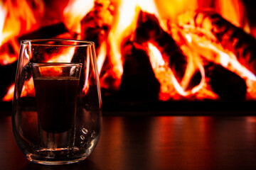 A beautiful glass with a drink near the fireplace. Firewood and fire. Glass and liquid.