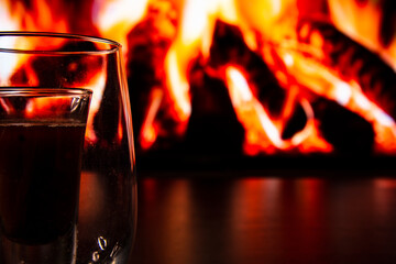 A beautiful glass with a drink near the fireplace. Firewood and fire. Glass and liquid.