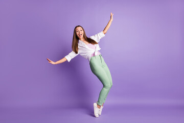 Photo of funky amazed girl stand tiptoes have fun wear sneakers pants white shirt isolated purple color background