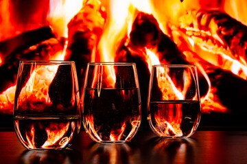 A beautiful glass with a drink near the fireplace. Firewood and fire. Glass and liquid.