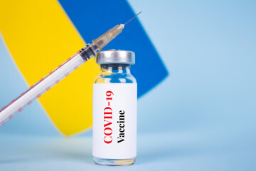 COVID-19 vaccine vial against Ukrainian flag on blue background with copy space for text - coronavirus vaccine doses, vaccination in Ukraine concept, selective focus