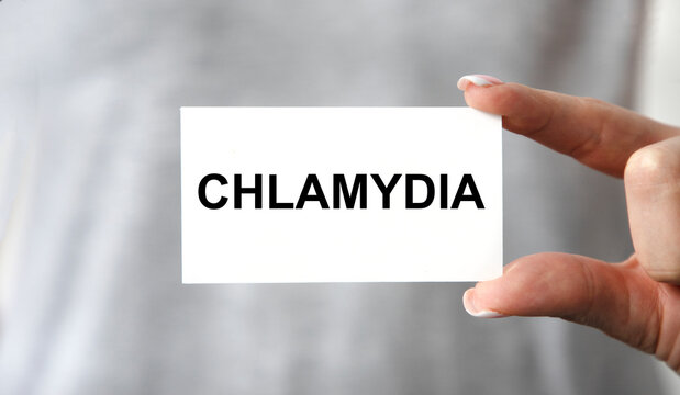 The girl holds a business card with CHLAMYDIA tacts in front of her.