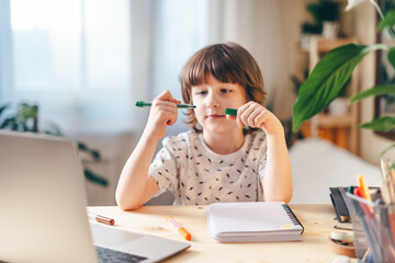 Distance learning online education. Caucasian smile kid boy studying at home with laptop and doing school homework. Thinking child siting at table with notebook. Back to school.