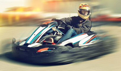 Young female in helmet driving car for karting in sport club outdoor