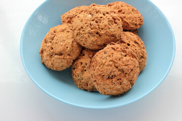 Homemade oatmeal cookies in a blue bowl on white table. Overhead view of oat biscuits on white background with copy space