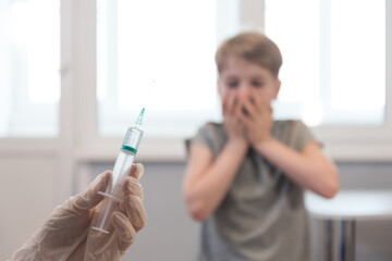 The child looks at the syringe in horror. Fear of injection. Emotions, unwillingness to get...