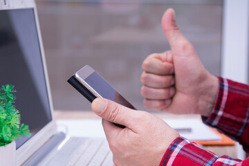 man with thumb raised making ok sign with mobile phone and laptop