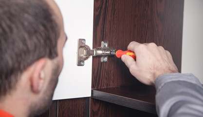 Man assembling cabinet hinge. Using screwdriver. Repair furniture