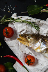 Smoked Fish on a cutting board. Ingredients for cooking: lemon, herbs, chili pepper and sea salt on a dark background
