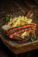 Grill house concept. Grilled, roasted tasty sausage with french fries on the old wooden cutting board.