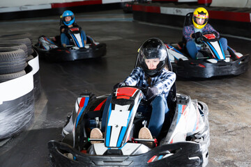 Group of male and females in helmets driving racing cars at kart track.