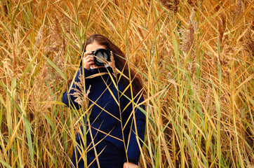 A girl photographer in a blue jacket, photographing the autumn nature through the grass.