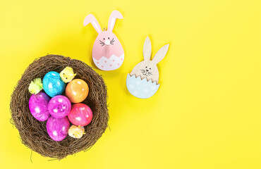 Easter eggs in nest and wooden decorative bunny on yellow background.