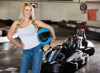 Fototapeta na wymiar Portrait of female racer holding helmet in her hand on kart track