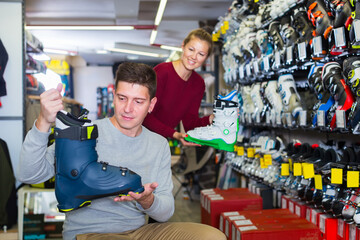 Fototapeta premium Woman assistant is helping man to trying on ski boots in store.