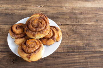 Cinnabon buns with sugar and cinnamon on a white plate on wooden background