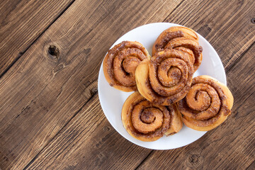 Cinnabon buns. Freshly baked cinnamon roll with spices and cocoa filling and coffee or cappuccino on white serving plate on wooden background with copy space. Swedish breakfast.