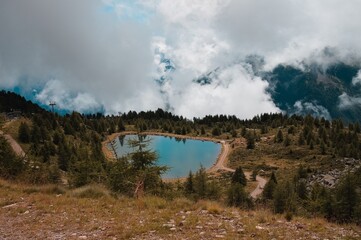 An alpine lake on the italian alps in the middle of a forest with clouds in the background (Peio,...