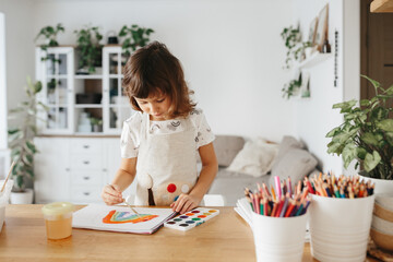 Kids painting watercolor rainbows at table at home