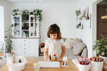Kids painting watercolor rainbows at table at home