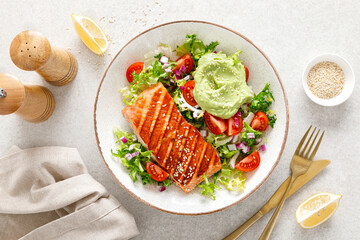 Grilled salmon fish fillet and fresh green lettuce vegetable tomato salad with avocado guacamole....