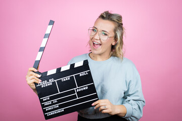 Young caucasian woman wearing sweatshirt over pink background holding clapperboard very happy...