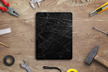 Repair broken tablet concept. Tablet with smashed disolay on work desk with tools beside. Top view,...