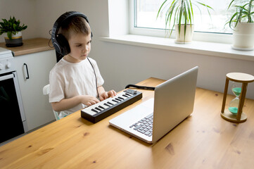 Preschooler boy in headphones learns to play the musical keyboard online. Distance learning to play the piano. Online music lessons.