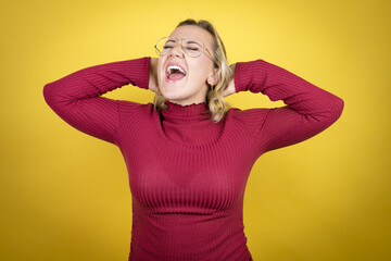 Young caucasian woman wearing casual red t-shirt over yellow background relaxing and stretching, arms and hands behind head and neck smiling happy