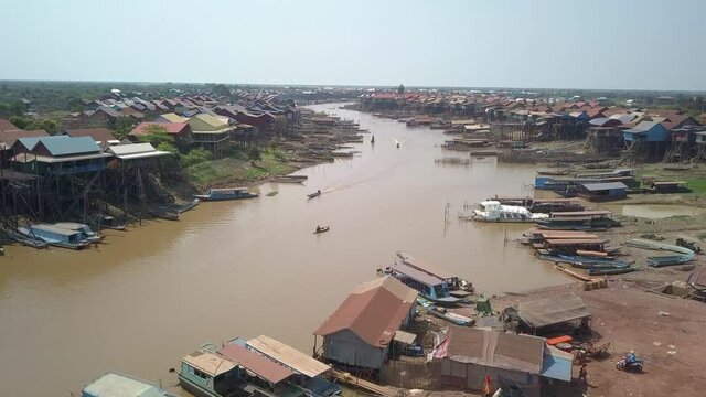 aerial drone shot of long tail fishing boats sailing through a floating village in the Tonle sap river during the dry season