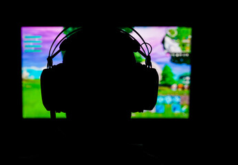 Silhouette of a young gamer wearing a headset while playing a popular battle royale game. Blurred background.