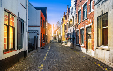 Narrow cobblestone street with traditional houses in medieval city center of Bruges, Belgium.