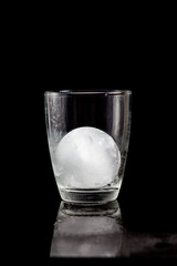 ice ball inside cocktail glass on a reflective black table.