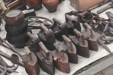 Old rusty original houseware. Outdated charcoal irons, pots and various retro items on sale. Toned