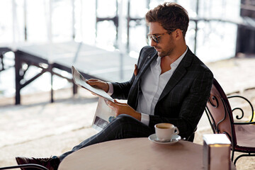 Handsome man drinking coffee and reading newspaper in cafe