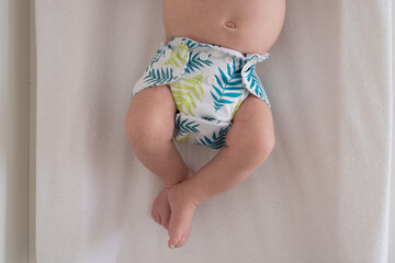 A baby lying on a bed with the focus on the baby's legs and cloth diaper with a pretty green leaf...