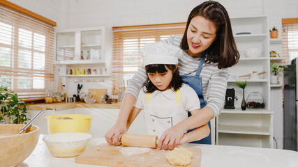 Happy smiling young Asian Japanese family with preschool kids have fun cooking baking pastry or pie for breakfast meal in modern kitchen home in the morning. Doing bakery knead dough and bake cookies.