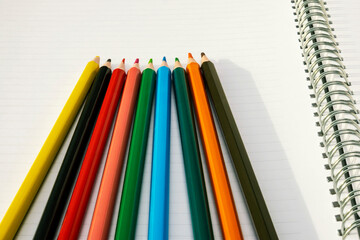 Pencils of different colors lie on an open drawing notebook. Copy space.