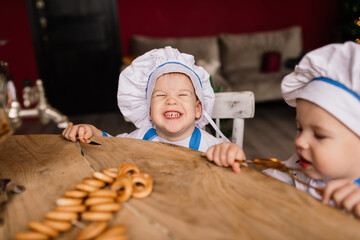 Little cute cook with cutlery sitting on a kitchen, twin brothers, tangerine, bagels