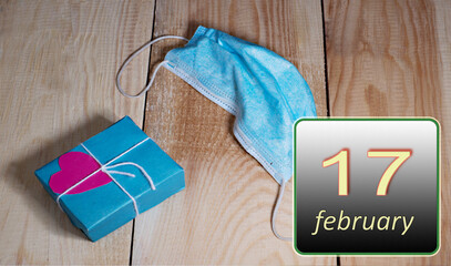 February 17, 17th day of month.Medical mask from covid 19 and box with gift for Valentine's Day lie on wooden boards Winter month.Day of the year concept.