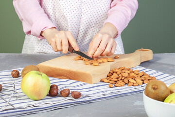 
Close-up of woman chopping almonds on cutting wooden board at kitchen table at home